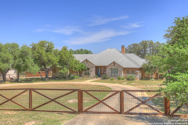 view of front of house with a front lawn, a gate, stone siding, a chimney, and metal roof