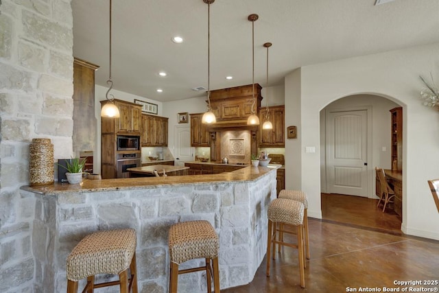 kitchen featuring concrete floors, a kitchen breakfast bar, brown cabinets, arched walkways, and appliances with stainless steel finishes