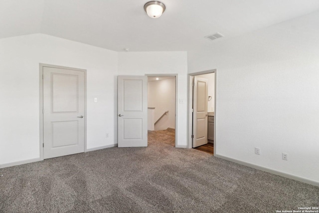 unfurnished bedroom featuring ensuite bathroom, baseboards, visible vents, carpet, and lofted ceiling