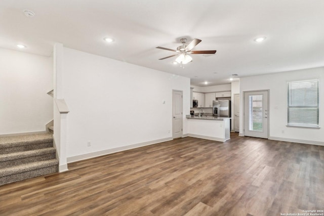 unfurnished living room with dark wood-style flooring, a ceiling fan, stairs, and a sink