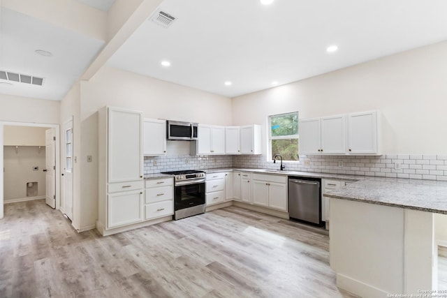 kitchen with light stone counters, visible vents, a sink, a peninsula, and appliances with stainless steel finishes