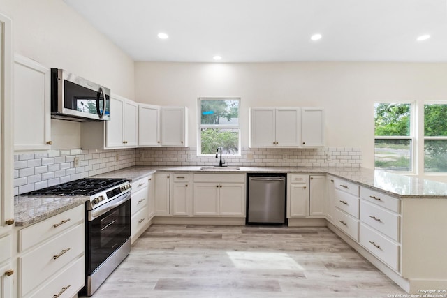 kitchen with white cabinets, a peninsula, a sink, light stone countertops, and appliances with stainless steel finishes