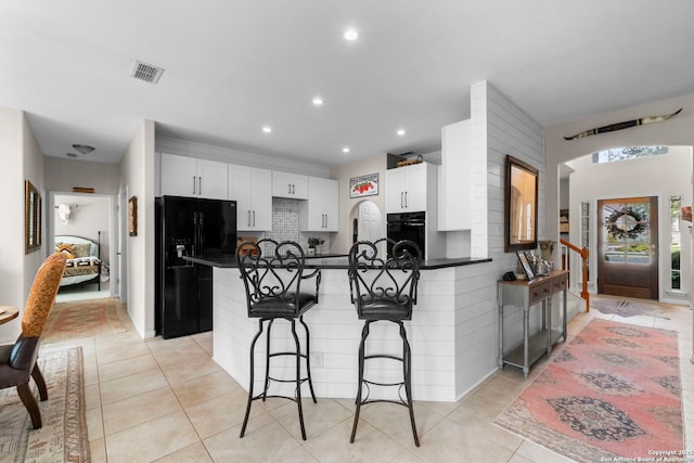 kitchen featuring a peninsula, a breakfast bar, dark countertops, and black appliances