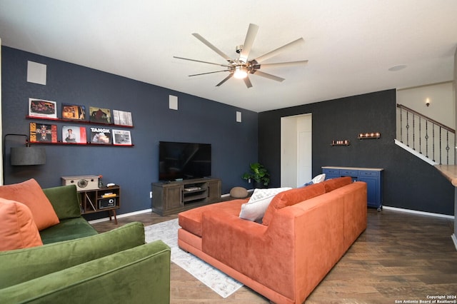 living area featuring baseboards, an accent wall, wood finished floors, ceiling fan, and stairway
