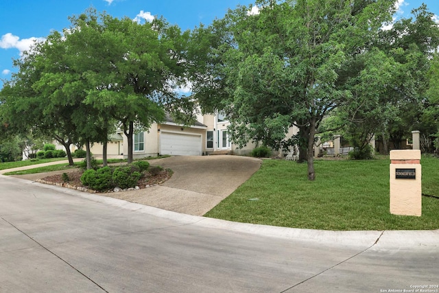 view of property hidden behind natural elements featuring a garage, driveway, a front lawn, and stucco siding