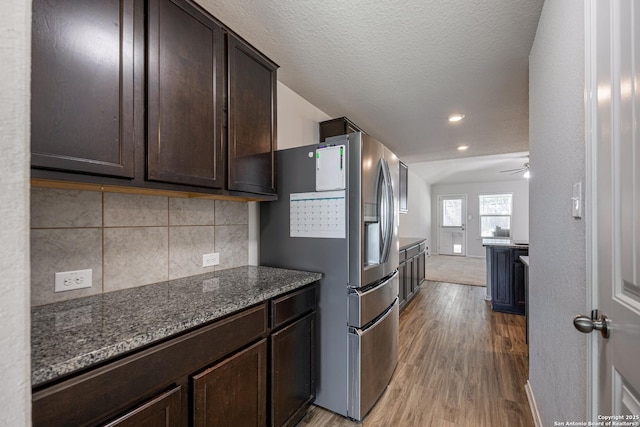 kitchen featuring lofted ceiling, dark brown cabinets, light wood-type flooring, stainless steel refrigerator with ice dispenser, and backsplash