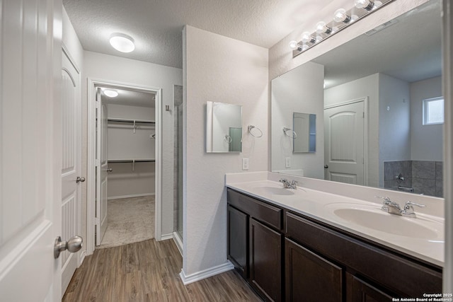 bathroom with double vanity, a sink, a walk in closet, and wood finished floors