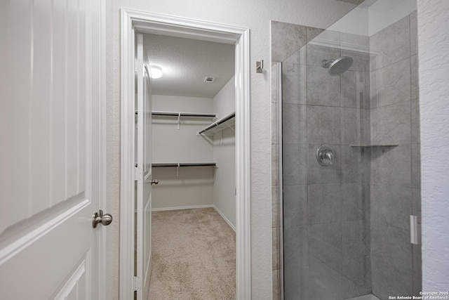 full bathroom with a walk in closet, a textured ceiling, baseboards, visible vents, and tiled shower