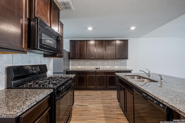 kitchen with dark brown cabinetry, light wood-type flooring, a sink, dark stone countertops, and black appliances
