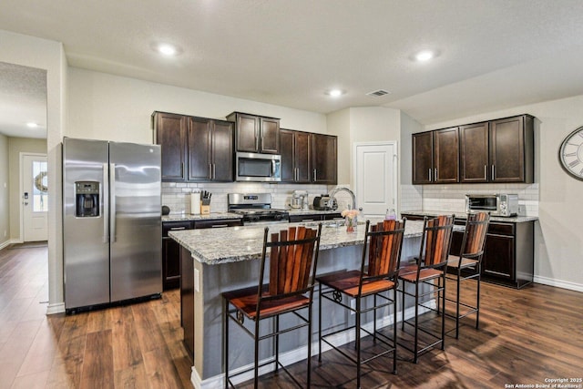 kitchen featuring backsplash, dark brown cabinets, appliances with stainless steel finishes, and a breakfast bar