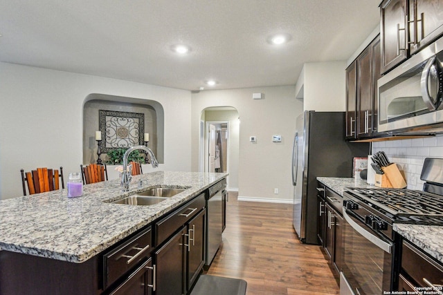 kitchen featuring dark wood-style floors, a sink, arched walkways, tasteful backsplash, and appliances with stainless steel finishes
