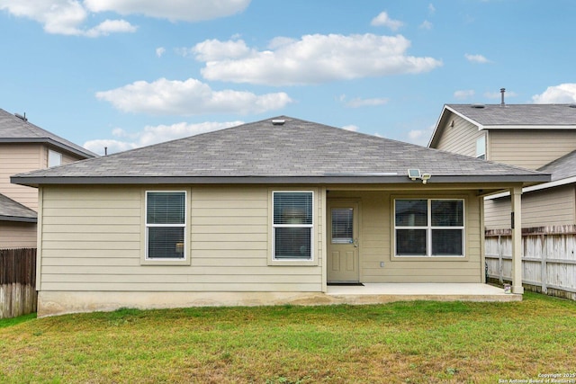 rear view of house featuring a lawn, a shingled roof, a patio, and fence
