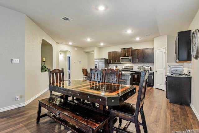 dining space with arched walkways, dark wood-style flooring, visible vents, and recessed lighting