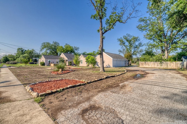 view of front facade featuring a detached garage, dirt driveway, and fence