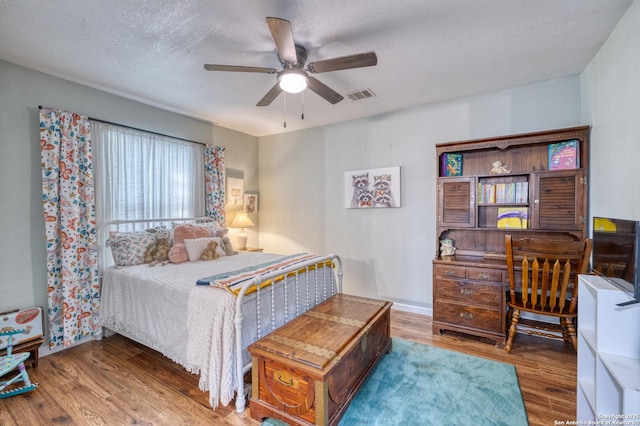 bedroom with a ceiling fan, wood finished floors, visible vents, and a textured ceiling