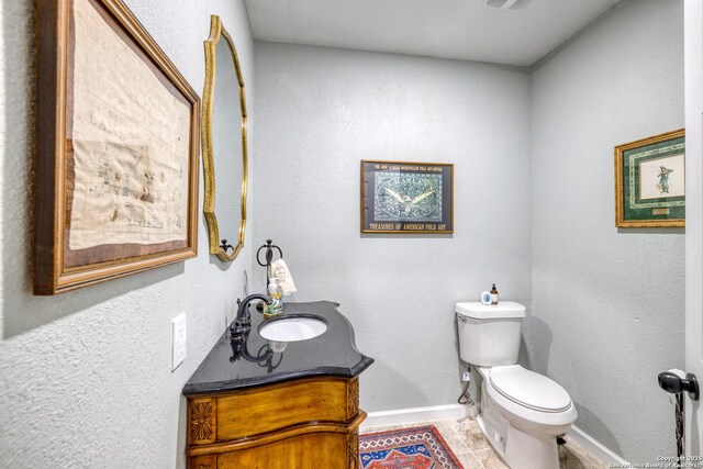 half bathroom featuring tile patterned floors, baseboards, vanity, and toilet
