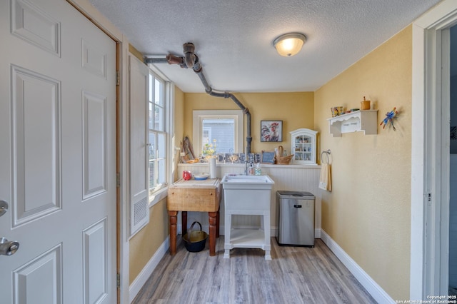 laundry area with wood finished floors, a textured ceiling, baseboards, and a sink