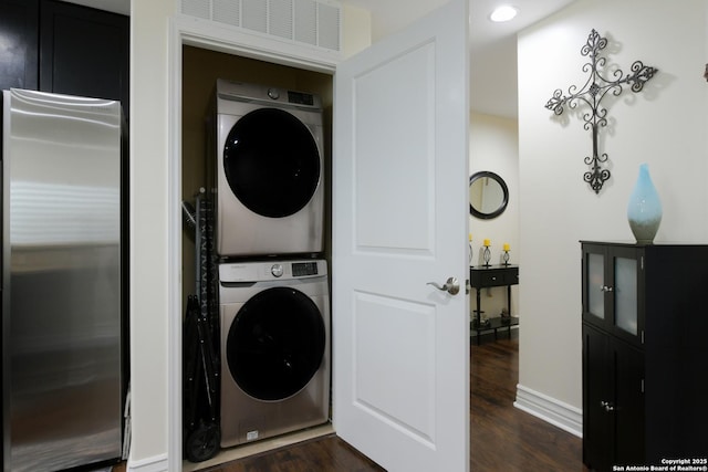 laundry room featuring stacked washer and clothes dryer, visible vents, baseboards, dark wood-style flooring, and laundry area