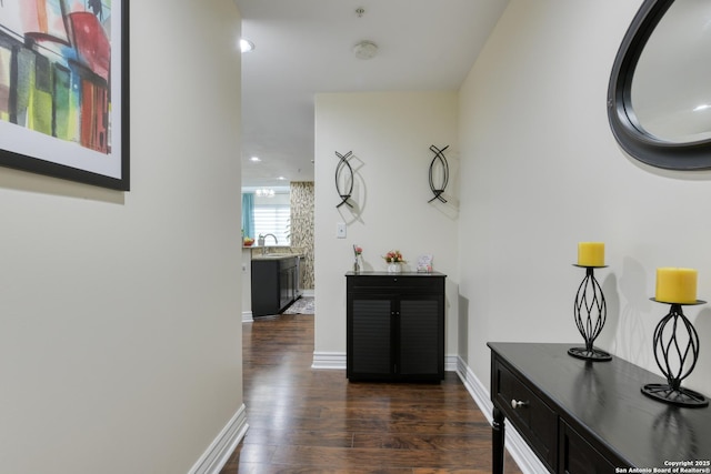 hallway with dark wood-style floors, baseboards, recessed lighting, and a sink