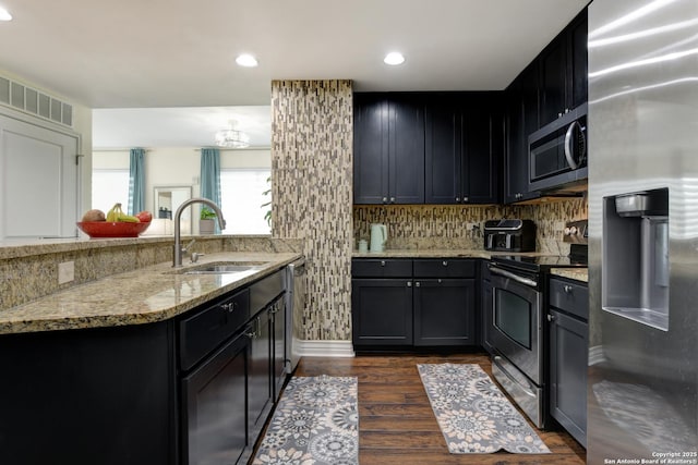 kitchen featuring a sink, dark wood-style flooring, stainless steel appliances, a peninsula, and light stone counters