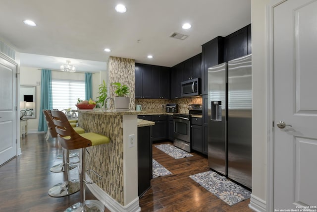 kitchen with a breakfast bar area, tasteful backsplash, visible vents, stainless steel appliances, and dark wood-style floors