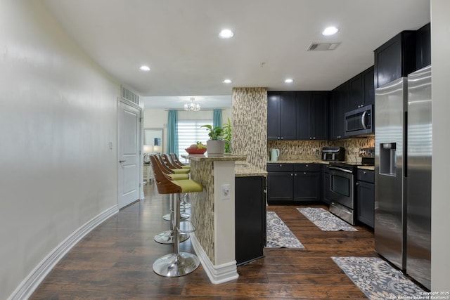 kitchen with decorative backsplash, stainless steel appliances, dark wood-style flooring, a kitchen bar, and visible vents
