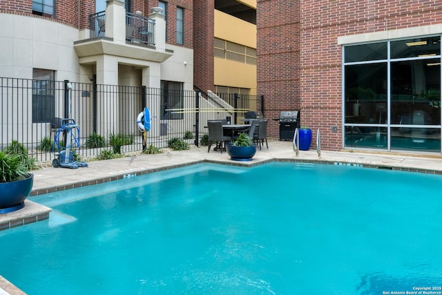 community pool with a patio, fence, and area for grilling