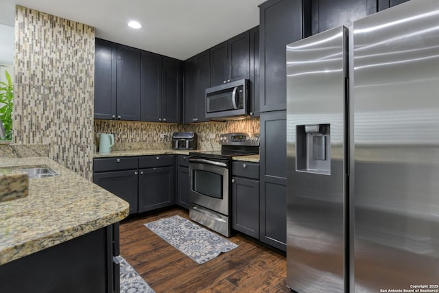 kitchen featuring tasteful backsplash, a sink, stainless steel appliances, dark wood-style flooring, and light stone countertops