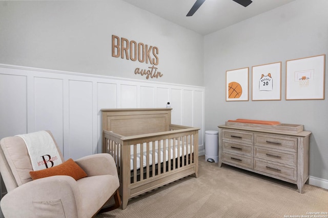 bedroom with a crib, a wainscoted wall, light colored carpet, and a decorative wall