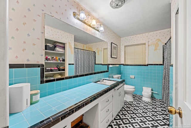bathroom featuring tile walls, wallpapered walls, and a wainscoted wall