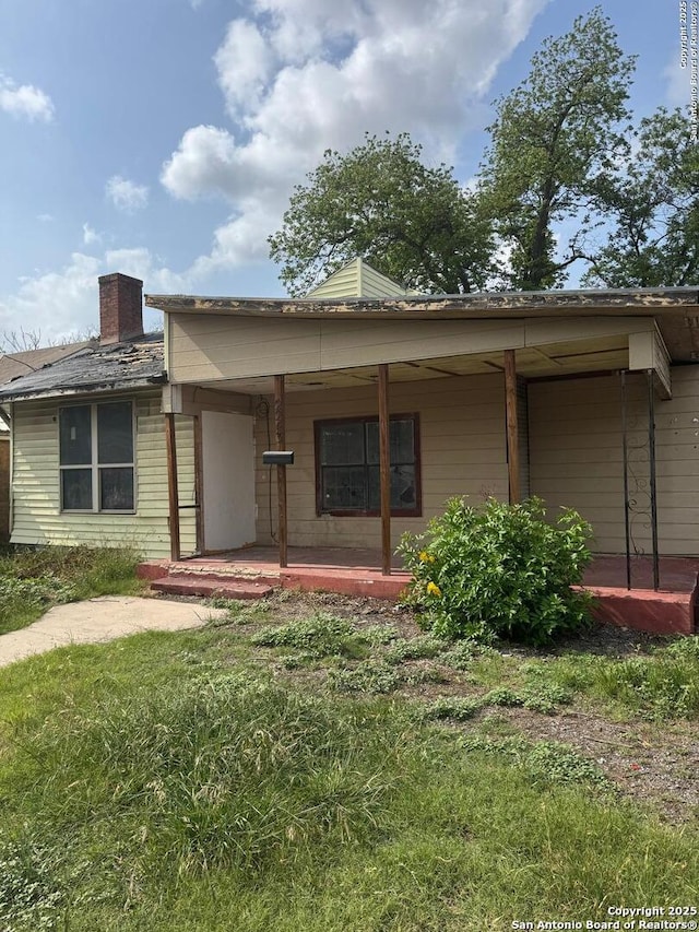 view of front of property with covered porch, a chimney, and an attached carport