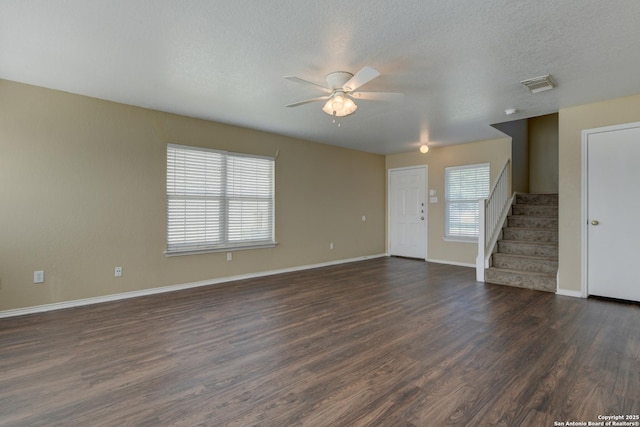 unfurnished living room with stairway, a ceiling fan, healthy amount of natural light, and dark wood-style floors