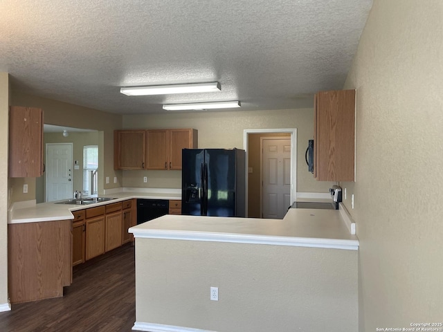 kitchen with black appliances, a peninsula, dark wood-type flooring, a textured ceiling, and light countertops