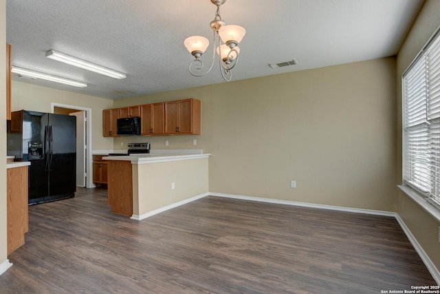 kitchen with black appliances, a peninsula, brown cabinets, a chandelier, and dark wood finished floors