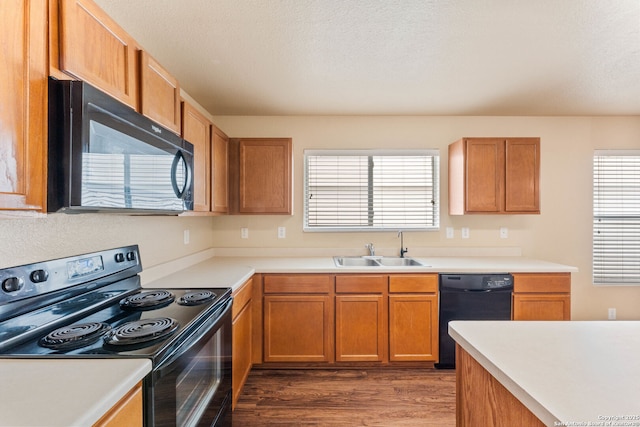 kitchen with wood finished floors, a sink, brown cabinetry, black appliances, and light countertops