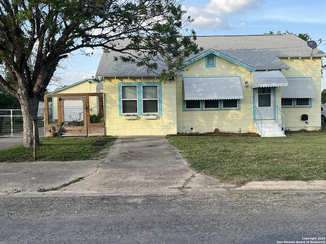 bungalow with entry steps, a front lawn, roof with shingles, and fence