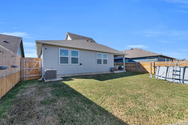 rear view of house featuring a fenced backyard, a gate, a yard, and central AC