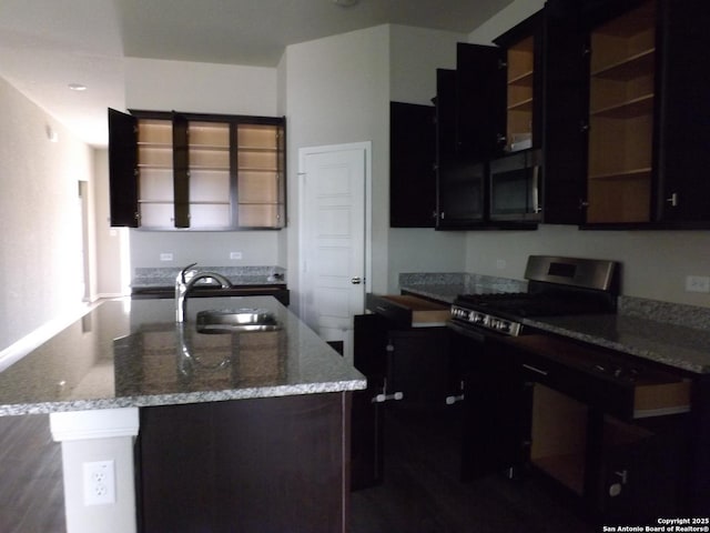 kitchen featuring light stone counters, open shelves, a sink, stainless steel gas range, and a kitchen island with sink