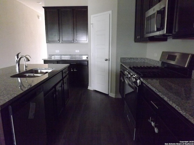 kitchen featuring dark stone counters, dark brown cabinets, a sink, appliances with stainless steel finishes, and dark wood-style floors