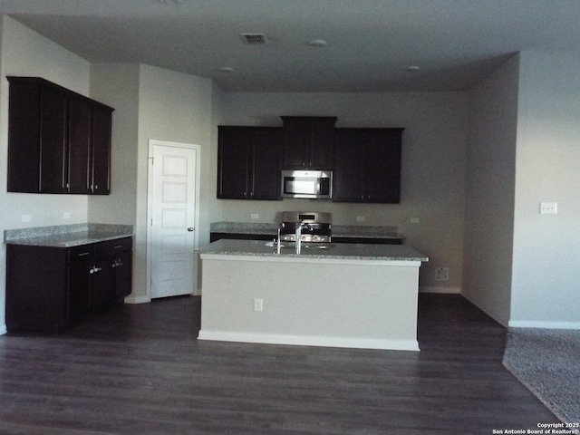 kitchen with stainless steel microwave, visible vents, baseboards, and dark wood-style flooring