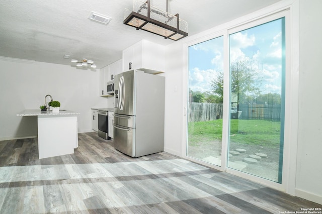 kitchen with a sink, light wood-type flooring, white cabinets, appliances with stainless steel finishes, and visible vents