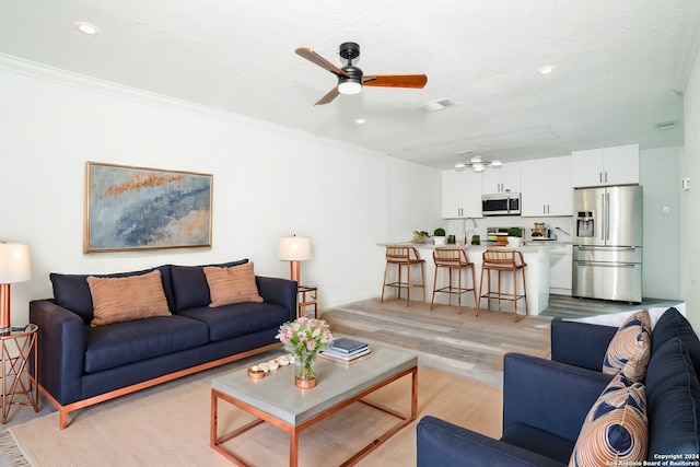 living room featuring light wood-type flooring, a ceiling fan, visible vents, and ornamental molding