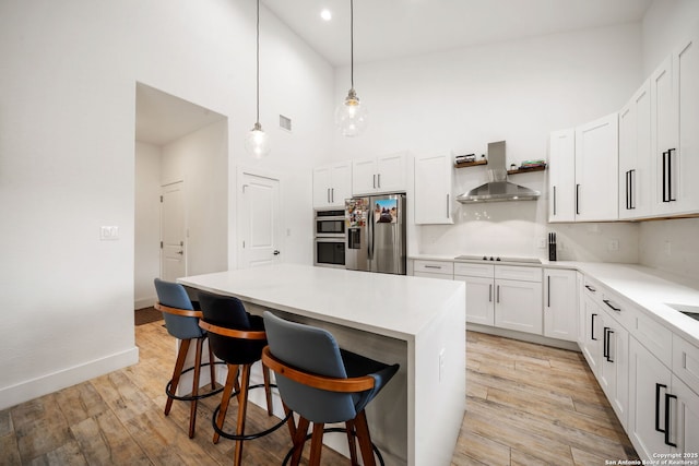2114 Village, San Antonio, TX 78251 - kitchen featuring stainless steel appliances, a center island, light wood-type flooring, a high ceiling, and wall chimney range hood