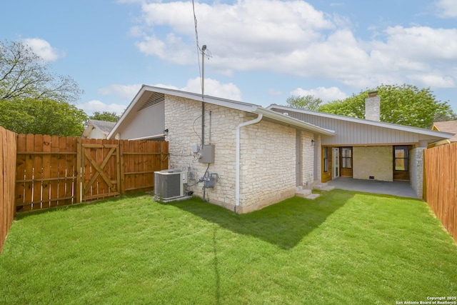 back of house featuring a chimney, a fenced backyard, a gate, cooling unit, and a lawn