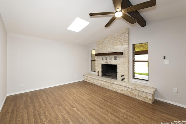 unfurnished living room featuring a fireplace, wood finished floors, vaulted ceiling with skylight, and baseboards