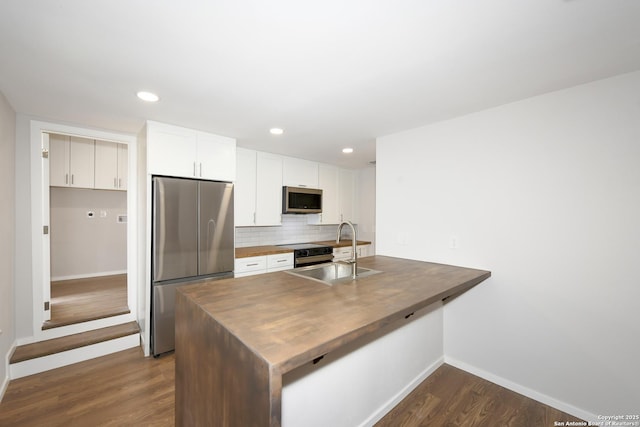 kitchen featuring wood counters, tasteful backsplash, a sink, stainless steel appliances, and baseboards
