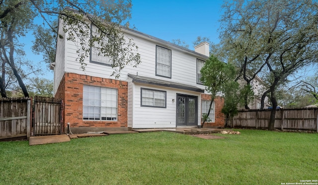 rear view of property featuring french doors, a fenced backyard, a chimney, brick siding, and a lawn