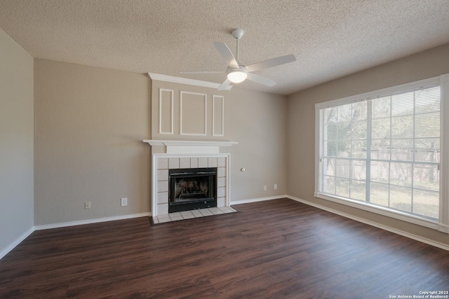 unfurnished living room featuring a tiled fireplace, dark wood-style floors, a textured ceiling, and ceiling fan