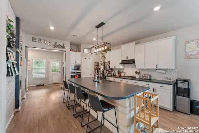 kitchen with dark countertops, a sink, appliances with stainless steel finishes, white cabinets, and under cabinet range hood