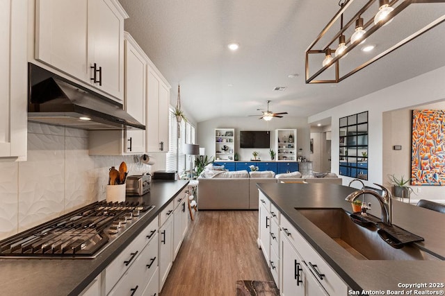 kitchen with under cabinet range hood, dark countertops, a ceiling fan, a sink, and stainless steel gas cooktop
